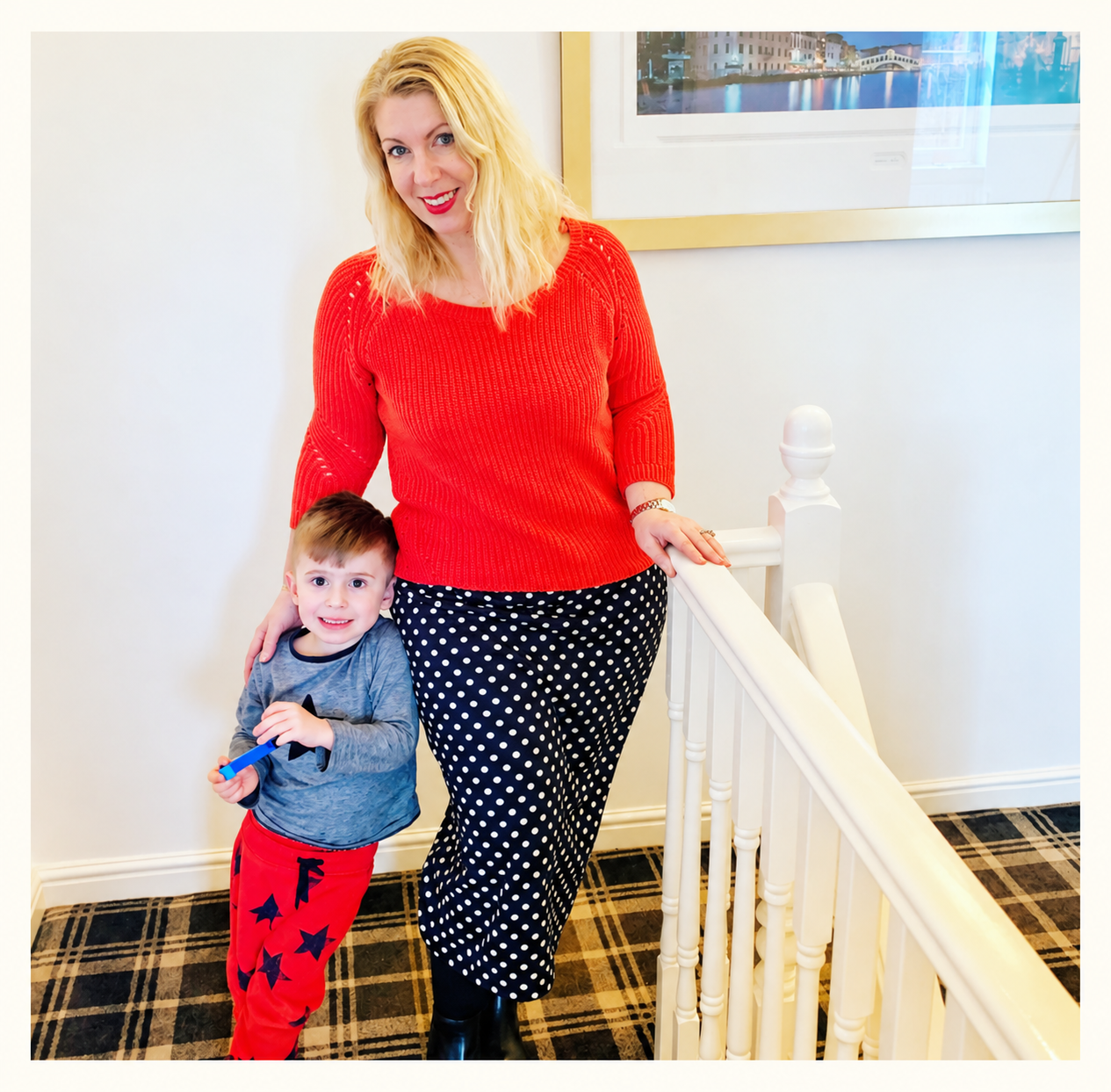 Saffron wearing red lipstick and a red jumper at home with a young Cyrus beside her.