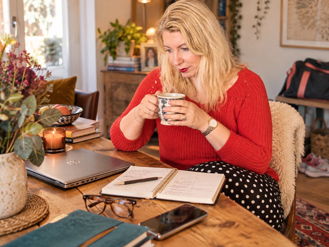 Saffron sits at her kitchen table with a coffee, notebook and laptop, reflecting on midlife, wellbeing and the year she stopped trying to fix herself.